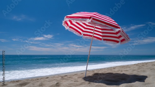 Red and white striped beach umbrella on sandy shore under clear blue sky