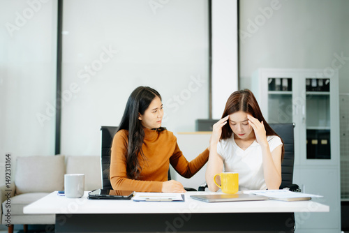 Asian woman comforts her distressed coworker in office. Concept of workplace stress, burnout, empathy, and emotional support in professional environments.