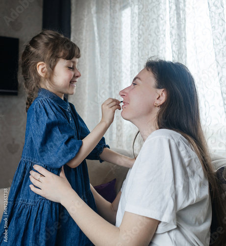 Daughter puts makeup on her mother face and plays around. Caring parent allows her child to paint her face. Happy childhood. Concept of loving family and fun. little girl doing her makeup