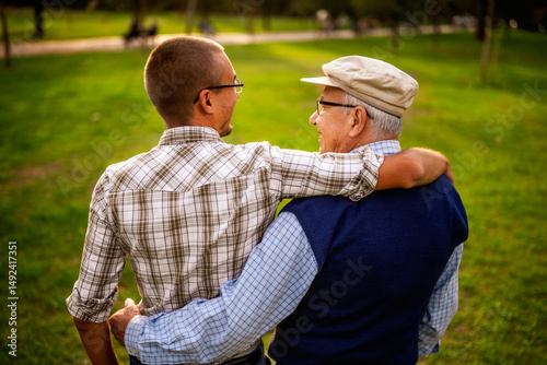 Rear view portrait of happy grandfather and grandson in park.