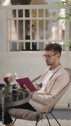 Man reading a book and relaxing at an outdoor cafe. He is enjoying a peaceful moment with his coffee and literature.