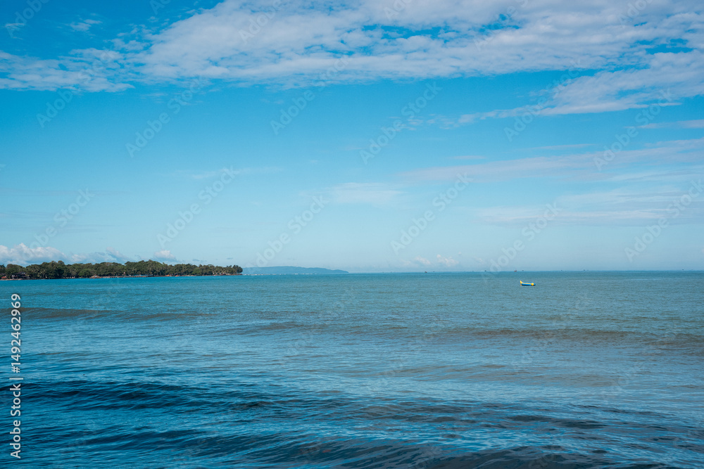 Obraz premium Tropical beach with calm blue sea, clear sky, and lush green island – perfect for travel, nature, and relaxation themes.