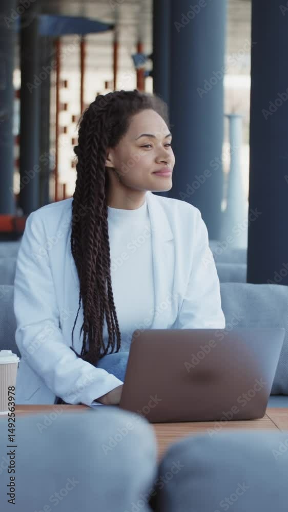 Happy young woman freelancer sitting on bench working with laptop in city on modern street. Typing on keyboard. Smiling. Slow motion