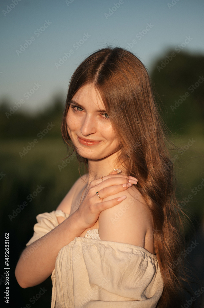 Fototapeta premium Elegant woman with long dark hair wearing a beige dress in a rural field at sunset, emotional close-up with warm backlight and soft tones, natural beauty in outdoor setting