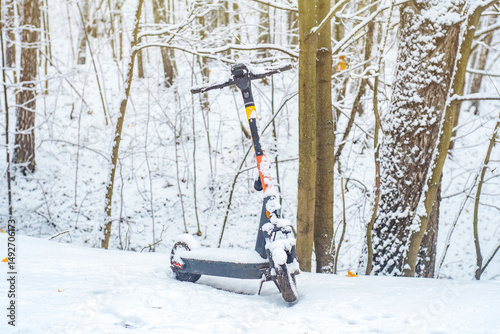 Public electric scooter covered with snow in the forest. Forgotten scooter in a winter park.