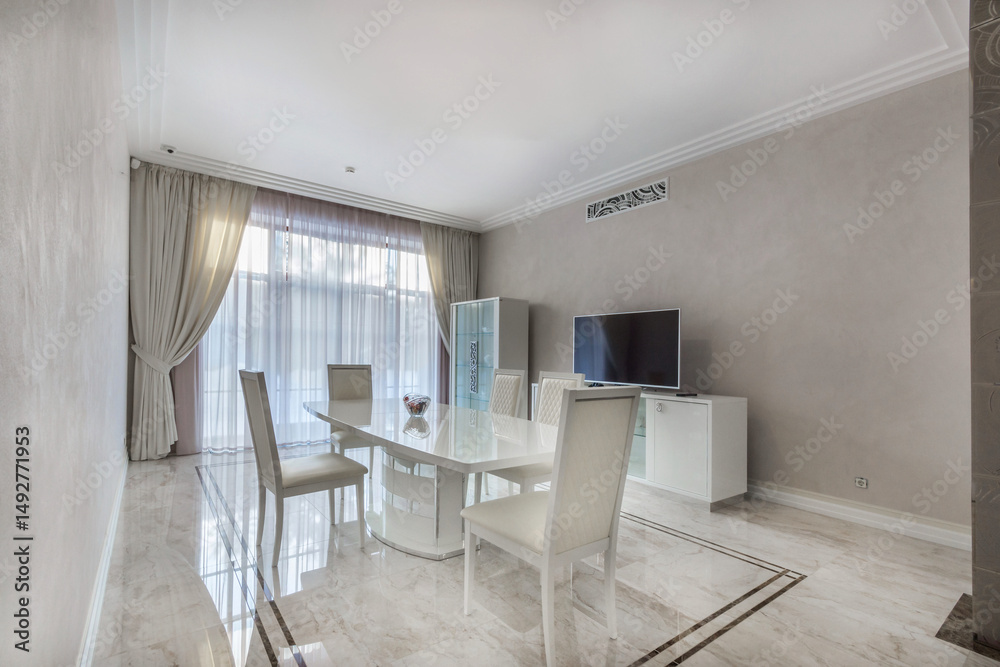 Fototapeta premium Elegant dining room of a country house with white furniture and a TV. The room with a panoramic window is decorated in pastel colors.