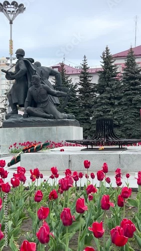 Sculpture to Soviet soldiers near the eternal flame against the background of red tulips in the city square