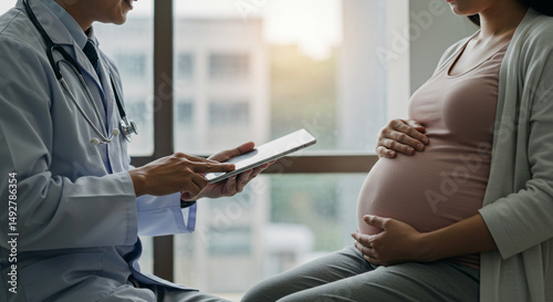 Doctor consulting with pregnant woman holding tablet in office with window background medical scene