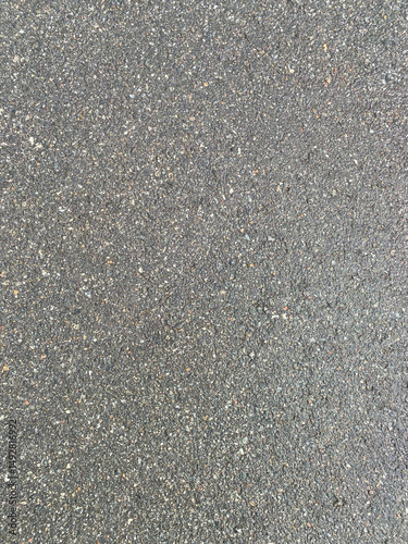 Close-up texture of gray asphalt road surface with small stones and cracks, detailed grunge background for construction and design