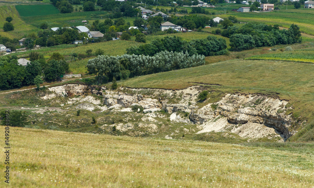 Obraz premium Rural landscape with eroded limestone cliffs and distant village houses in summer