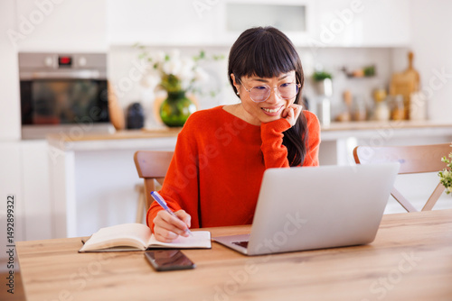 Mature woman taking notes while having online meeting using laptop computer