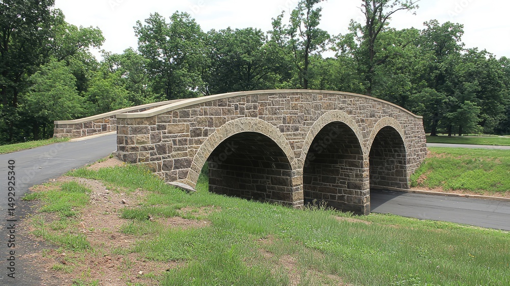 Fototapeta premium Stone Arch Bridge Spanning Road in Lush Green Park Setting