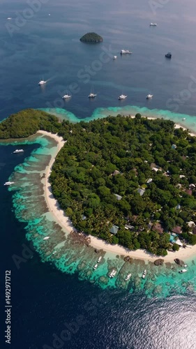 An aerial view of a tropical island surrounded by crystal clear water with boats scattered around. This scene creates a feeling of relaxation and escape.