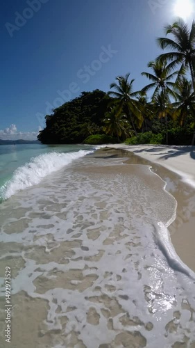 Tropical beach paradise with gentle waves lapping the shore, palm trees swaying in the breeze, under a vibrant blue sky 