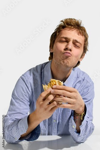 Fotografie Young man in striped shirt closing eyes in satisfaction while chewing shawarma roll, hands holding wrap with visible sauce and filling