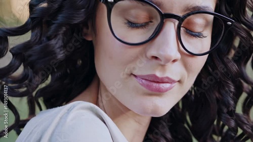 a pensive portrait of a woman wearing eyeglasses, with a look of quiet contemplation, eyes closed, and a gentle smile