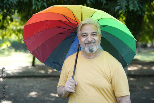 Monsoon Bonanza Concept. Indian Senior man under rainbow umbrella and walking outdoor for relax freedom. Asian elder man  enjoy monsoon with nature, fresh air and stunning views