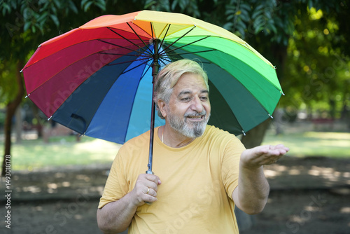 Monsoon Bonanza Concept. Indian Senior man under rainbow umbrella and walking outdoor for relax freedom. Asian elder man  enjoy monsoon with nature, fresh air and stunning views