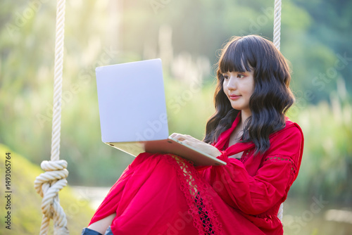 Beautiful confident asian businesswoman working with laptop, Hands typing keyboard. Online chat. Spend free time on the swing. Sunrise beam in the beautiful park.