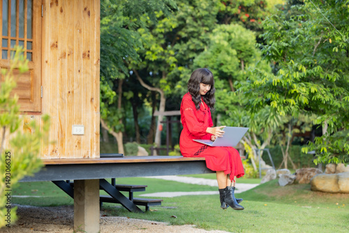 Focused asian woman watching webinar on laptop, writing blog or email, remotely online work in her home garden surrounded by plants. Nature view of green leaf in garden under sunlight in the afternoon