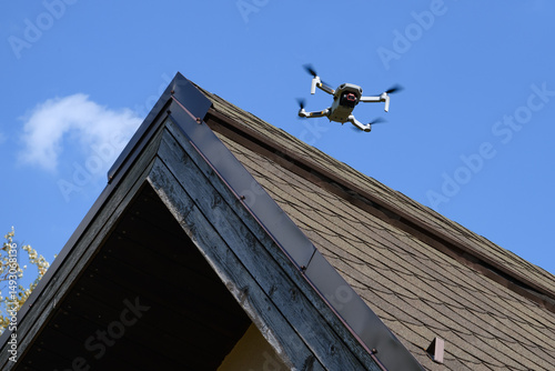 Drone in the air inspecting the roof over the house closeup blue sky