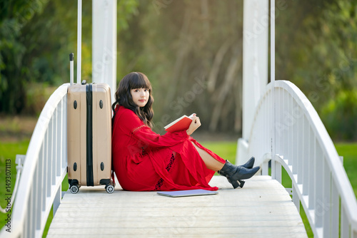 Woman traveler with suitcase ready for summer journey vacation trip looking at camera and reading book. 