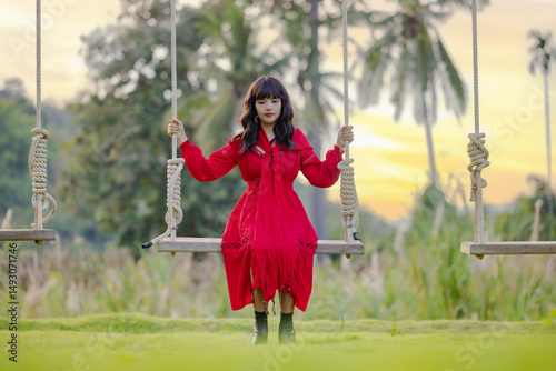 Beautiful young asian woman on a swinging on a swing at nature garden. Outdoor portrait of a smiling happy girl. Young woman enjoying freedom.
