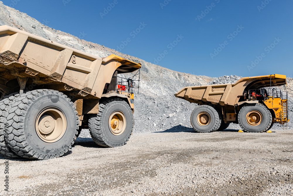 Obraz premium Massive Dump Trucks in Open-Pit Mine Under Clear Blue Sky