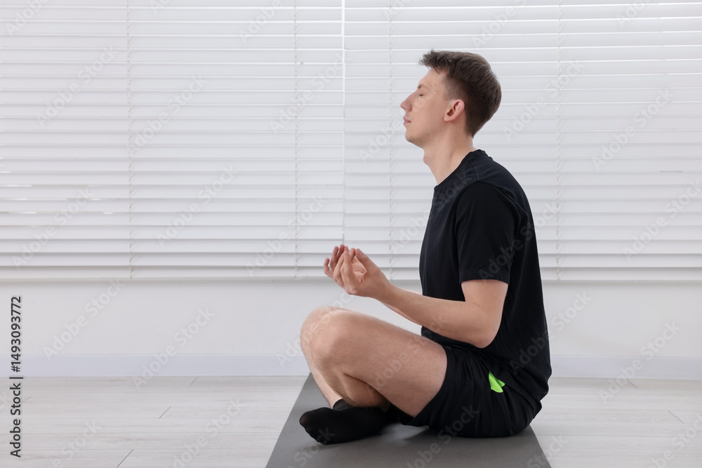 Fototapeta premium Young man practicing yoga on mat at home. Space for text