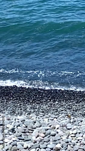 Tranquil blue ocean waves and pebble beach nature background.Water washing on shoreline over pebbles on bright sunny day. Summer,vacation, travel, relax concept,
vertical video