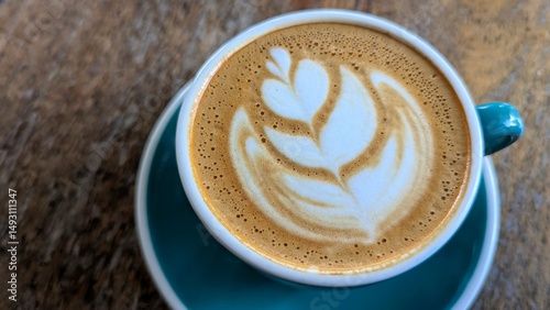 Closeup of delicious golden flat white coffee with latte art in teal cup and saucer on rustic wooden table