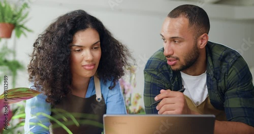 Close up. Woman working at laptop together with man florist using an online service to accepting orders delivery. African American young couple florists in aprons working in flower store and talking