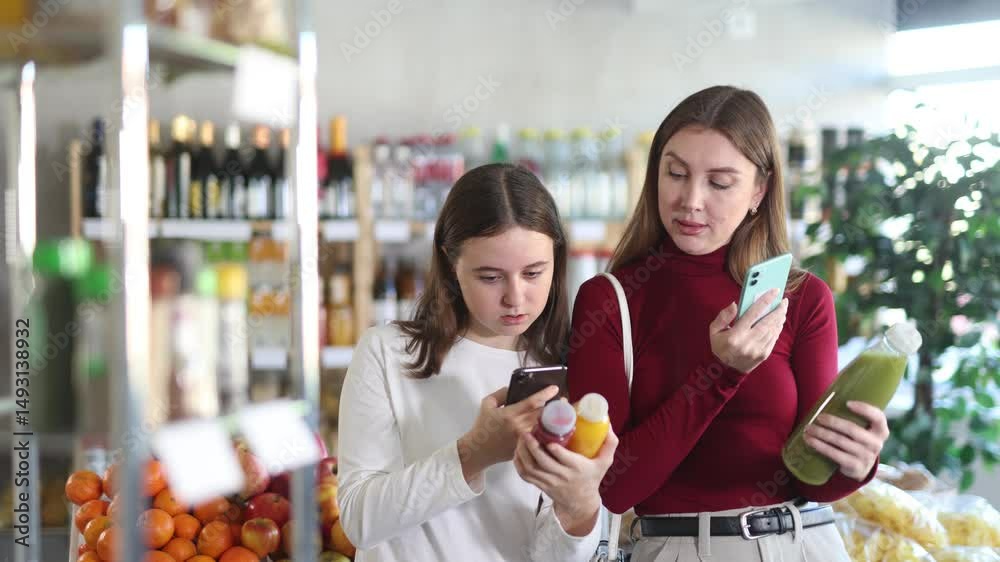 Mother and teenager daughter scan the barcode on smoothie bottles on mobile phones and find out the ingredients, calories and amount of sugar. Mother and daughter using an online app in a supermarket