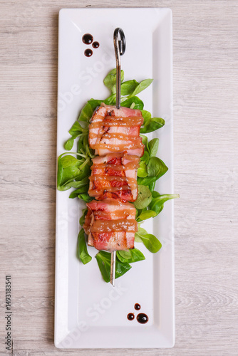 Tre pezzi di filetto di maiale avvolti nel bacon e infilati in uno spiedone di ferro e serviti come antipasto in una braceria photo