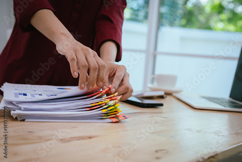 Close-up of businesswoman in office sorting through large amount of financial documents and files, filled with documents, accounts and reports.