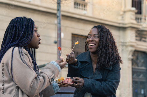 Two smiling friends sharing fruit outdoors in urban setting