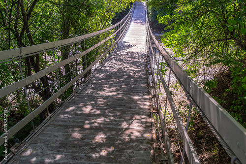 Suspended wooden bridge on steel cables over a mountain river. Suspension bridge in the city park. The passage point across the river.
