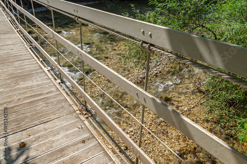 Suspended wooden bridge on steel cables over a mountain river. Suspension bridge in the city park. The passage point across the river.