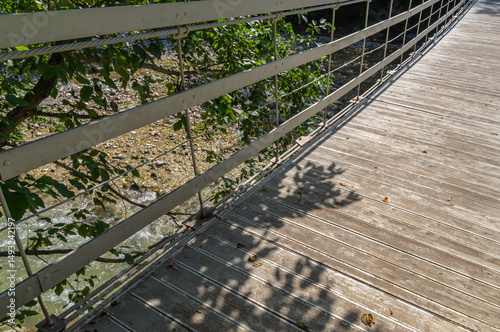 Suspended wooden bridge on steel cables over a mountain river. Suspension bridge in the city park. The passage point across the river.