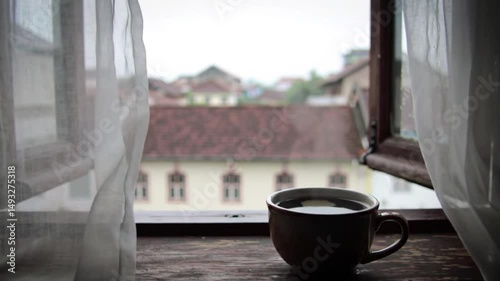 Steaming cup of hot coffee by window overlooking cold cityscape, cozy moment in winter urban setting
