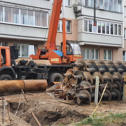 Crane lifting screw piles for building foundation.