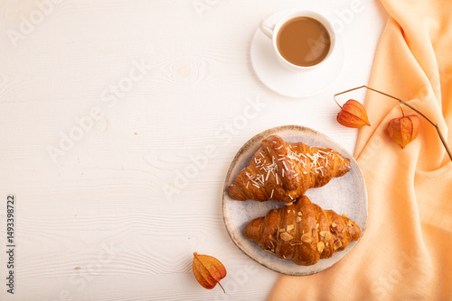 Croissant on blue plate on white wooden and orange textile, cup of coffee, top view, flat lay, copy space