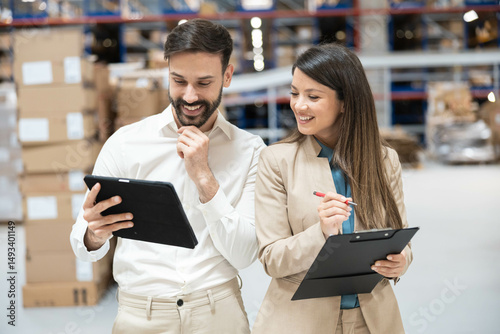 Two warehouse managers reviewing data on tablet and clipboard, smiling