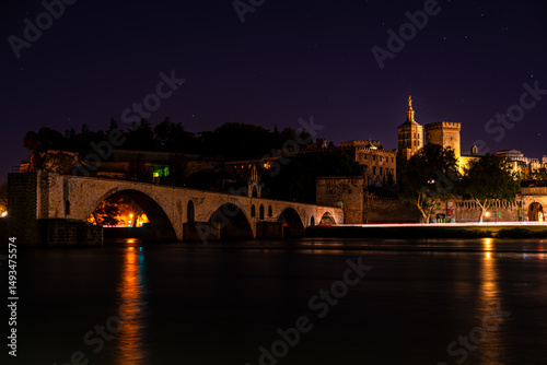 In Avignon, France, the medieval bridge of Saint-Bénézet and the illuminated Palais des Papes merge history with tranquility under the calm darkness of a Provençal night.