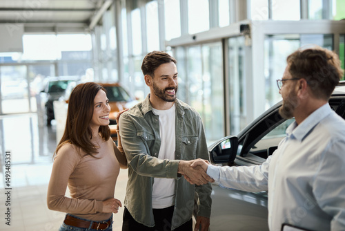 Happy young couple shaking hands with car salesperson in a showroom