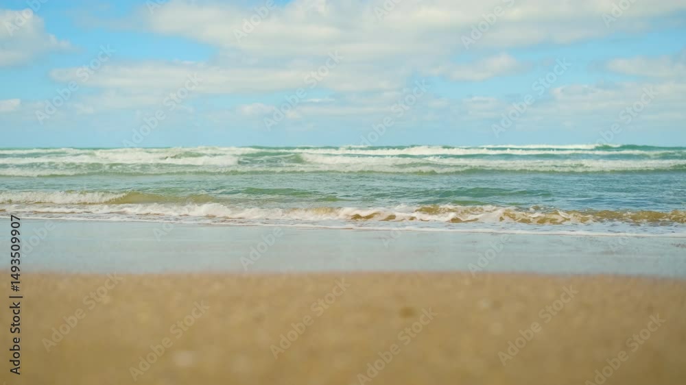 Sea waves roll on sandy shore in rhythmic motion, beach footage after a storm, waves attract attention with wild coastal energy and invite you to swim in sea, concept for advertising a beach holiday Sea waves roll on sandy shore in rhythmic motion, beach footage after a storm, waves attract attention with wild coastal energy and invite you to swim in sea, concept for advertising a beach holiday