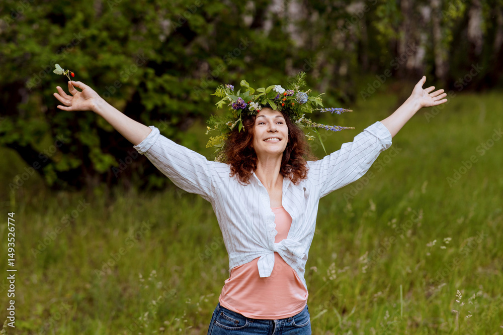 Cheerful adult woman reconnects with summer nature, enjoying the serene countryside. The female model stands in a wildflower wreath during a cultural celebration Cheerful adult woman reconnects with summer nature, enjoying the serene countryside. The female model stands in a wildflower wreath during a cultural celebration