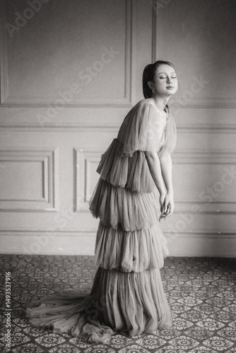 Elegant woman in a tiered tulle dress poses with eyes closed in a soft light studio