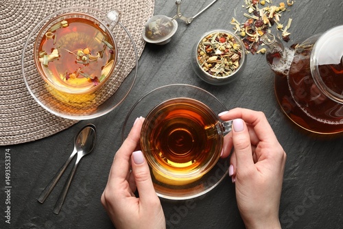 Foto Woman with aromatic herbal tea at black table, top view