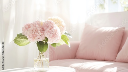 Elegant pink hydrangeas in a glass vase on a white table beside a soft couch in a bright living room